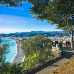 Widok na lazurowe morze i Niceę, stare miasto z promenadą. Ludzie podziwiają panoramę z tarasu widokowego.