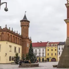 Rynek w Tarnowie zimową porą, z choinką i świątecznymi iluminacjami. W tle charakterystyczna wieża ratuszowa i kolorowe kamieniczki.