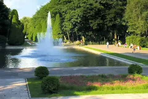 Park z fontanną i geometrycznie przyciętymi drzewami, przypominający ogrody w stylu Versailles.