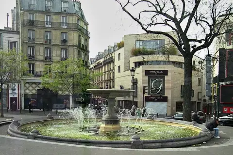 Fontanna na placu Pigalle w Paryżu, otoczona kamienicami i drzewami.