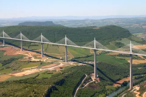 Najwyższy most w Europie, Viadukt Millau, przecina zieloną dolinę z imponującymi pylonami i stalowymi linami.