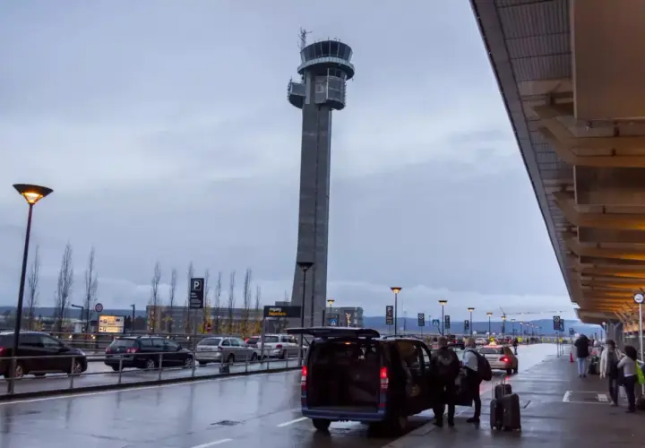 Wieża kontrolna lotniska Oslo Gardermoen, samochody i ludzie przy terminalu.