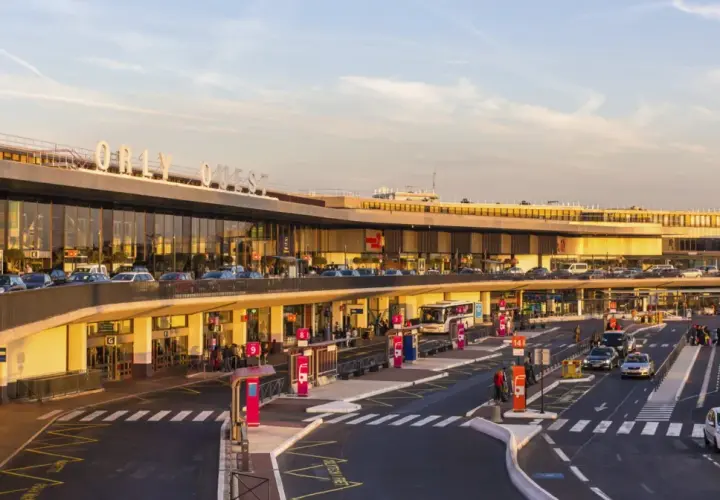 Orly Ouest, jedno z lotnisk we Francji, tętni życiem. Samochody i autobusy krążą przed nowoczesnym terminalem, a pasażerowie z bagażami czekają na odlot.