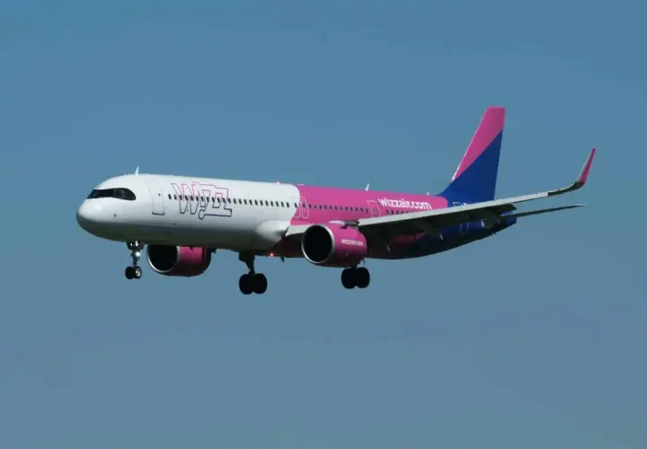 Samolot Wizz Air z różowym i niebieskim ogonem zbliża się do lądowania. W bagażniku rejestrowanym Wizzair zmieści się wszystko, czego potrzebujesz.