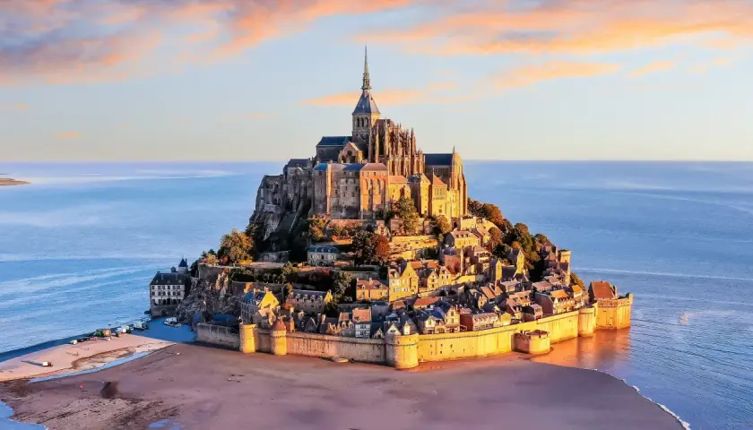 Bajkowy zamek na wodzie we Francji, Mont Saint-Michel, w blasku zachodzącego słońca, otoczony wodami oceanu.