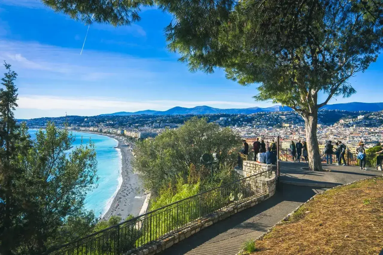 Widok na lazurowe morze i Niceę, stare miasto z promenadą. Ludzie podziwiają panoramę z tarasu widokowego.