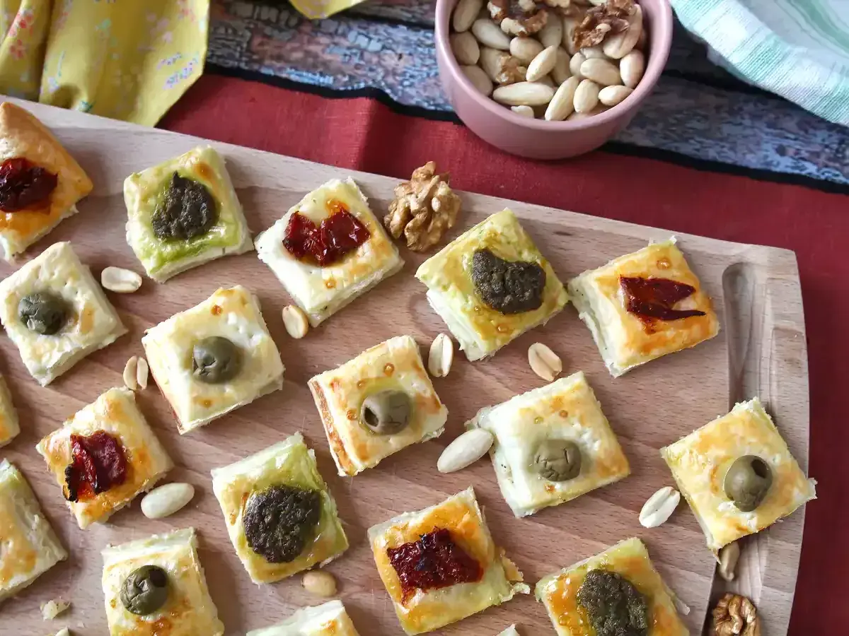 Pyszne przekąski francuskie z oliwkami, pesto i suszonymi pomidorami, ułożone na desce.