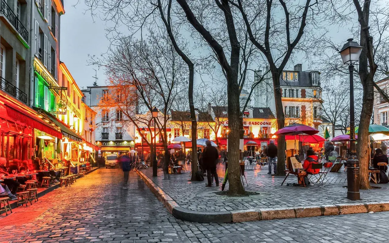 Wieczorny spacer po wzgórzu Montmartre. Brukowana ulica, kawiarnie, artyści malujący na placu.