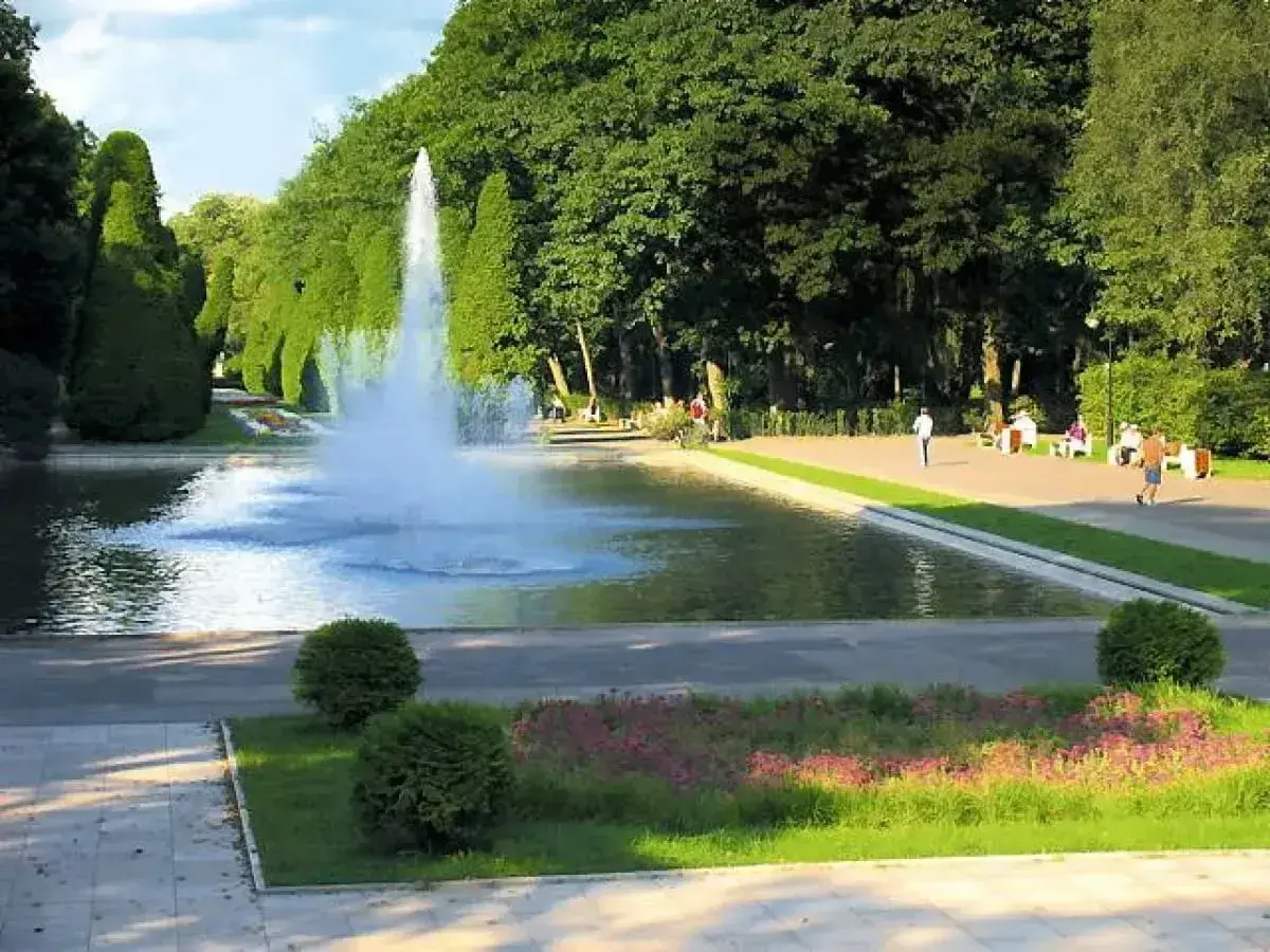 Park z fontanną i geometrycznie przyciętymi drzewami, przypominający ogrody w stylu Versailles.