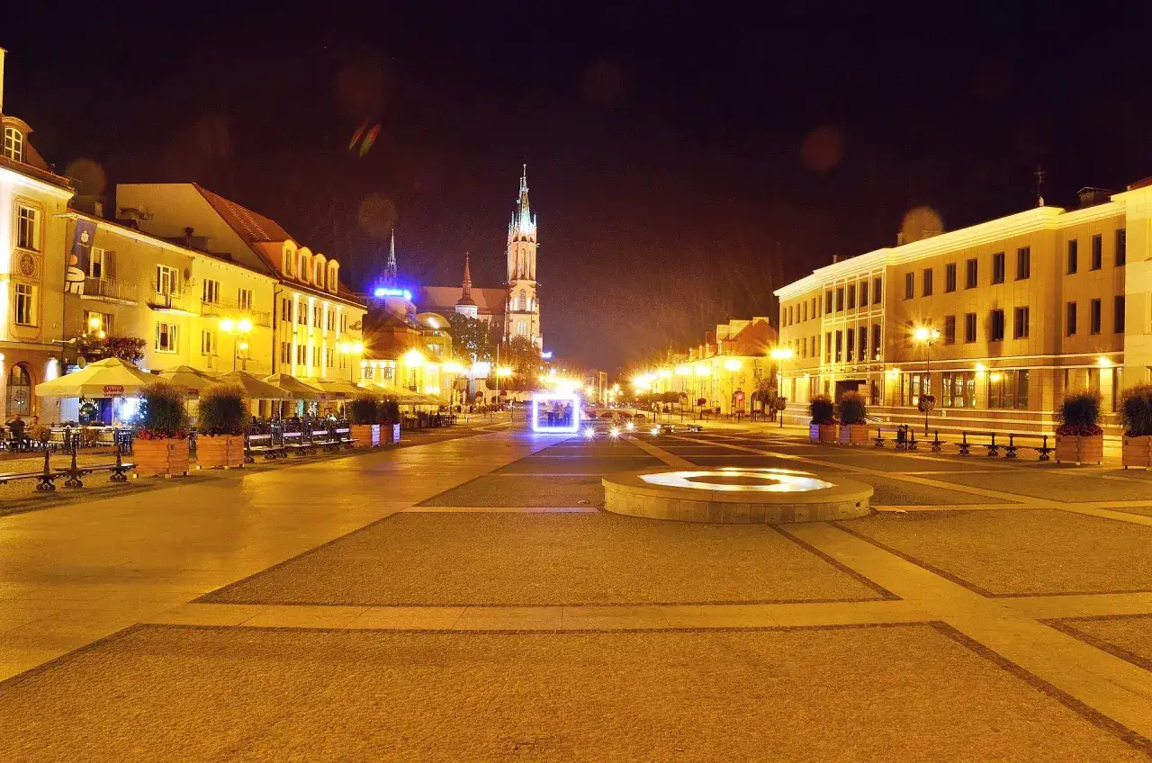 Nocny rynek Kościuszki w Białymstoku, oświetlony latarniami i neonami, z widoczną katedrą w tle.