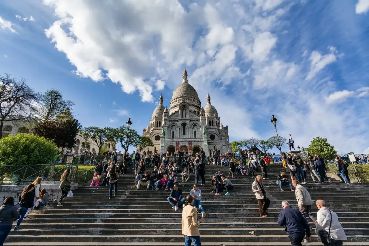 Tłum ludzi odpoczywa na schodach bazyliki Sacré-Cœur na wzgórzu Montmartre.