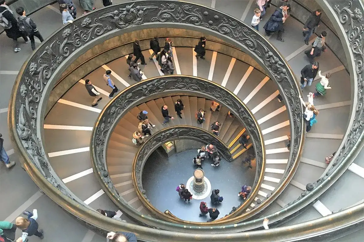 Watykan, Rzym. Tłum turystów schodzi po zabytkowych, spiralnych schodach Muzeum Watykańskiego.