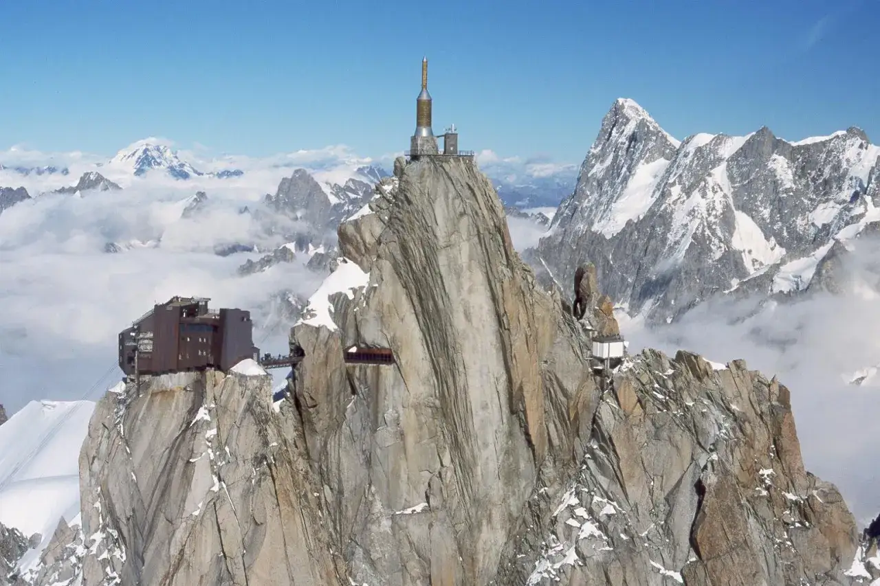 Wjazd na Mont Blanc: stacja kolejki linowej na skalistym szczycie, otoczona ośnieżonymi górami i chmurami.
