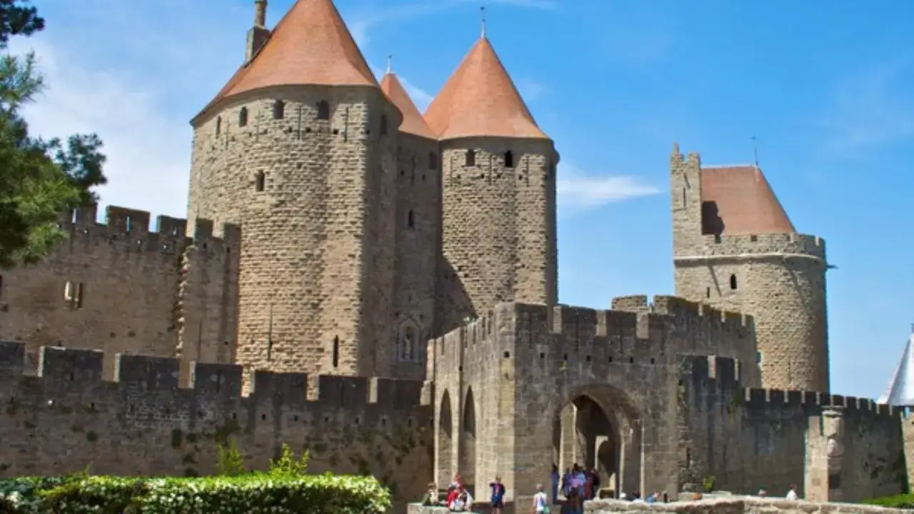 Kamienne mury i wieże średniowiecznego zamku Carcassonne, z charakterystycznymi stożkowymi dachami, pod błękitnym niebem.
